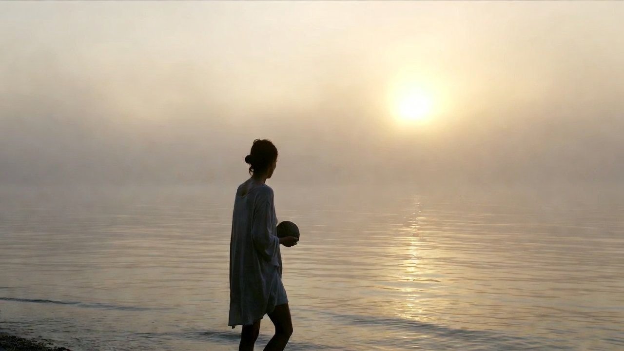 Person holding a smooth stone on a calm foggy shoreline at dawn, symbolizing emotional regulation and finding calm amid emotional waves